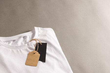 Folded white t shirt with tags with copy space on brown background. Fashion, clothes, colour and...