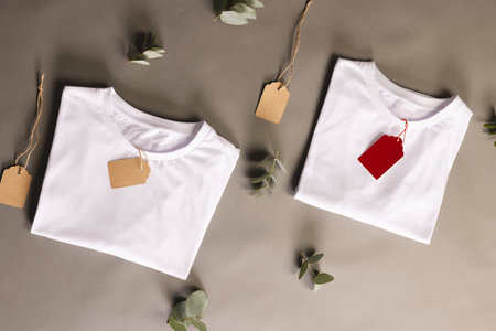 Folded white t shirts with tags and leaves with copy space on brown background. Fashion, clothes,...