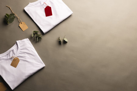 Folded white t shirts with tags and leaves with copy space on brown background. Fashion, clothes, colour and fabric concept.の写真素材