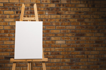 White canvas on wooden easel and copy space on brick wall background. Signage, writing space and advertising concept.の写真素材