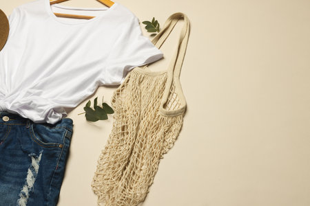 Flat lay of white t shirt, sunhat, net bag and denim skirt with copy space on cream background....