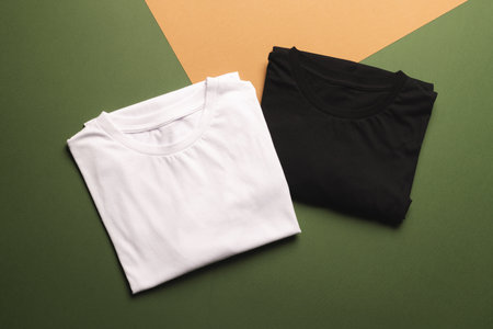 Close up of folded white and black t shirts and copy space on green to orange background. Fashion, clothes, colour and fabric concept.の写真素材