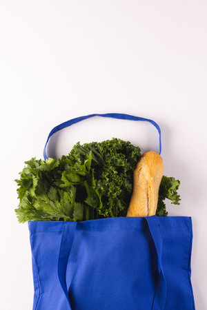 Blue canvas bag with baguette and green salad vegetables and copy space on white background. Fresh...
