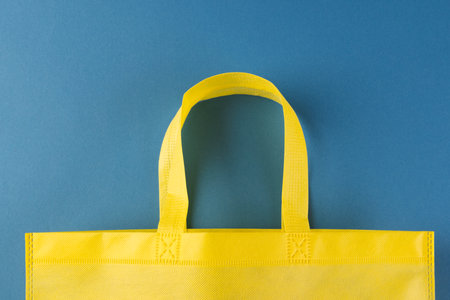 Close up of yellow canvas bag with copy space on blue background. Shopping, bag, colour, fabric, texture and materials concept.の写真素材