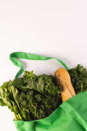Green canvas bag with baguette and green salad vegetables and copy space on white background. Fresh food, shopping, bag, colour, fabric, texture and materials concept.の写真素材