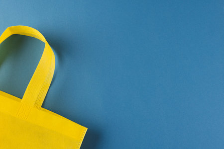 Close up of yellow canvas bag with copy space on blue background. Shopping, bag, colour, fabric,...