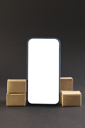 Vertical image of smartphone with blank screen and cardboard boxes, copy space on black background. Cyber monday, cyber shopping, retail, technology, electronic device and communication concept.の写真素材