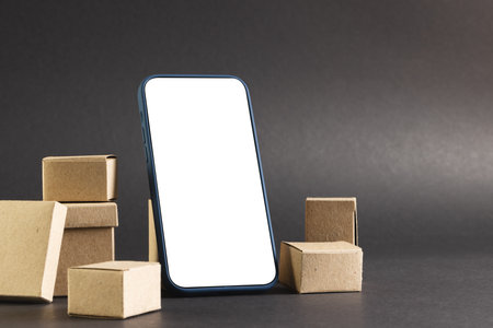 Smartphone with blank screen and cardboard boxes with copy space on black background. Cyber monday, cyber shopping, retail, technology, electronic device and communication concept.の写真素材