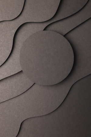 Vertical image of circle of black paper with copy space on black waves of paper on black background....