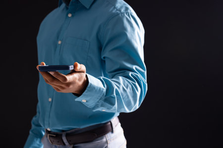 Biracial businessman using smartphone on black background. Technology, digital networks, global connections and communication metaverse.の写真素材