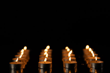 Rows of lit tea candles with copy space on black background. Flame, fire, colour and light concept.の写真素材