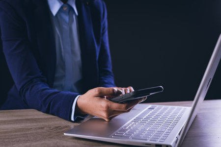 Biracial businesswoman using smartphone and laptop on black background. Technology, digital...