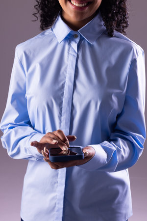 Vertical image of biracial businesswoman using smartphone with copy space on grey background. Technology, digital networks, global connections and communication metaverse.の写真素材