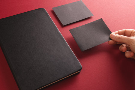 Black notebook and caucasian woman holding black paper card on red background. Paper, writing,...