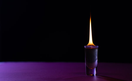 Lit candle in purple glass container with copy space on purple and black background. Flame, fire,...