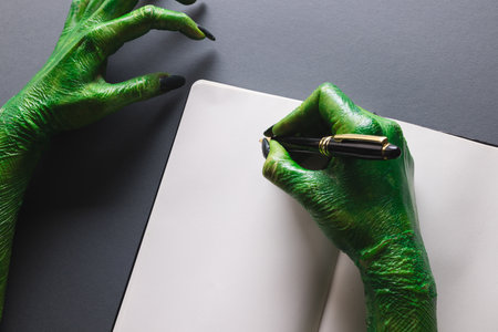Green monster hands writing notebook with copy space on grey background. Halloween, tradition and...