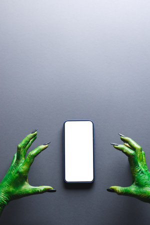Vertical image of green monster hands making with smartphone with copy space on grey background. Halloween, tradition and celebration concept.の写真素材