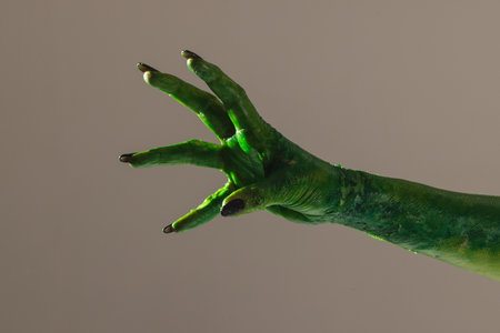 Green monster hand with black nails reaching on grey background. Halloween, tradition and...