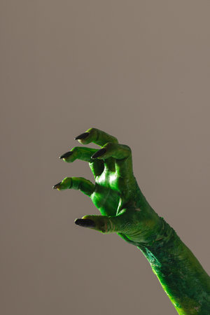 Vertical image of green monster hand with black nails making gesture on grey background. Halloween, tradition and celebration concept.の写真素材