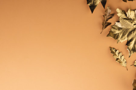 Metallic gold autumn leaves with copy space on orange background. Fall, autumn, halloween, tradition...