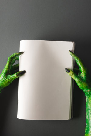 Vertical image of green monster hands holding notebook with copy space on grey background. Halloween, tradition and celebration concept.の写真素材