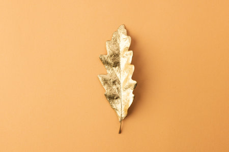 Metallic gold autumn leaf with copy space on orange background. Fall, autumn, halloween, tradition...