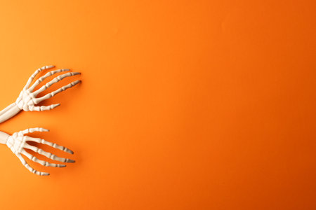 Plastic skeleton hands with copy space on orange background. Fall, autumn, halloween, tradition and celebration concept.の写真素材