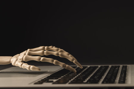 Plastic skeleton hand on laptop keyboard with copy space on black background. Fall, autumn, halloween, tradition and celebration concept.の写真素材