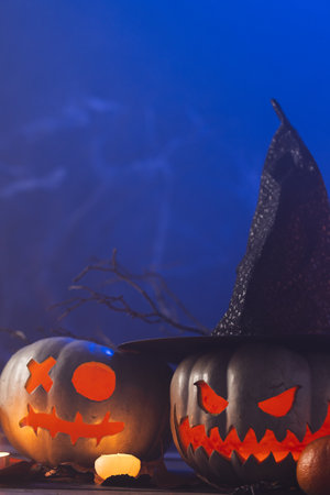 Vertical image of carved pumpkins and candle with copy space on blue background. Fall, autumn,...