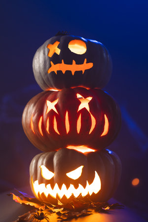 Vertical image of three illuminating carved pumpkins tower on blue background. Fall, autumn, halloween, tradition and celebration concept.の写真素材