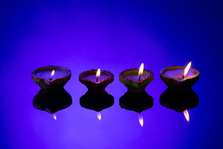Close up of four diwali candles with copy space on purple background. Diwali, festival of lights,...