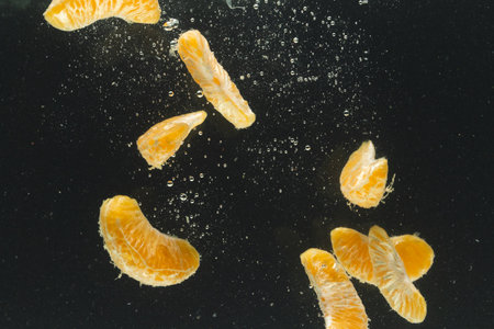 Close up of tangerine segments falling into water with copy space on black background. Fruit, vegan food and colour concept.の写真素材