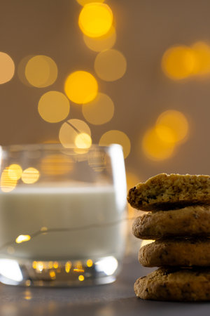 Vertical image of glass of milk and christmas cookies with copy space and fairy lights background. Sweets, christmas, tradition and celebration concept.の写真素材