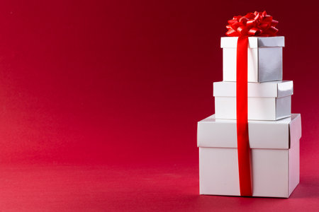 Stack of white christmas presents with red ribbon and copy space on red background. Presents,...