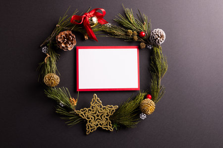 Christmas wreath with baubles and decorations with white card and copy space on black background....