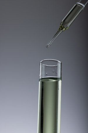 Vertical image of close up of laboratory test tube and pipette with copy space on grey background....