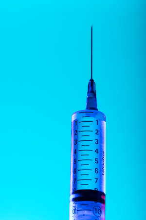 Vertical image of close up of syringe with needle and copy space on blue background. Laboratory,...