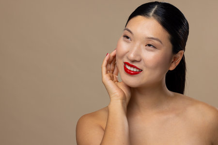 Asian woman wearing red lipstick and nail polish on beige background, copy space. Cosmetics, makeup, female fashion and beauty, unaltered.の写真素材