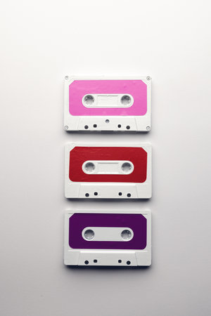 Overhead view of three colourful cassette tapes arranged on white background. Music, sound,...