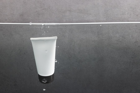 Beauty product tube falling into water with copy space background on grey background. Health and...