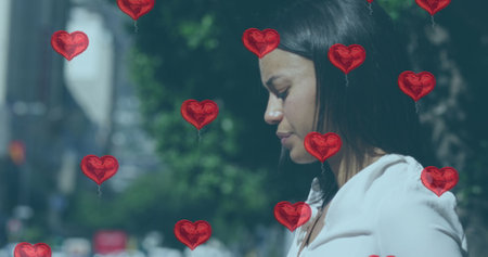 Biracial woman surrounded by heart balloons, with copy space. She's outdoors, reflecting on a romantic moment or celebration.の写真素材