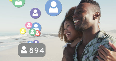 Profile icons with increasing numbers floating against african american couple smiling on the beach. social media networking and vacation conceptの写真素材