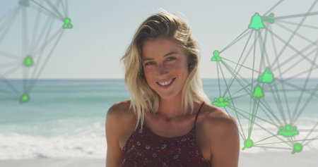 Image of spinning networks with social media digital icons over smiling woman on beach. digital interface, social media and global networking concept digitally generated image.の写真素材