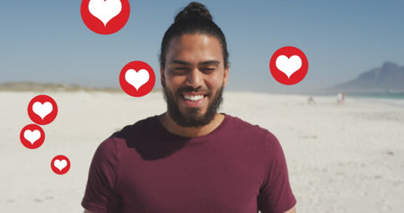 Image of social media red heart love icons over smiling man on beach. digital interface, social...