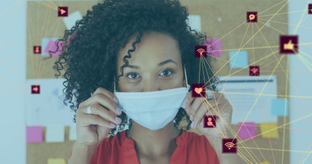 Image of net of connections with social icons with woman in office wearing face masks. Healthcare...