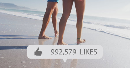 Image of speech bubble with thumbs up icon and numbers, low section of couple walking on beach. digital interface, social media and global network concept digitally generated image.の写真素材