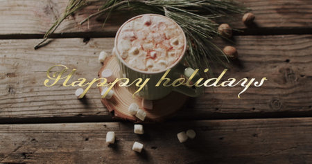 Happy holidays text in gold over christmas hot chocolate with marshmallows on wooden background....