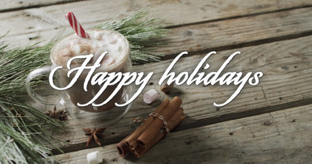 Happy holidays text in white over christmas hot chocolate and cinnamon sticks on wooden background....