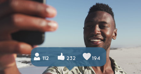 Image of people, thumbs up and heart icons over smiling man using smartphone on beach. digital...
