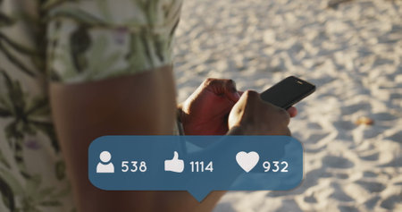 Image of people, thumbs up and heart icons with numbers over man using smartphone on beach. digital interface, social media and global technology concept digitally generated image.の写真素材